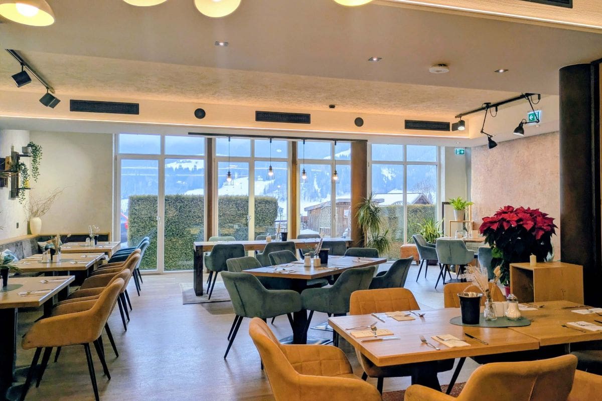 Frühstücksbereich im Julie's mit Holztischen, gemütlichen Sesseln und Fensterfront mit Blick auf Terrasse