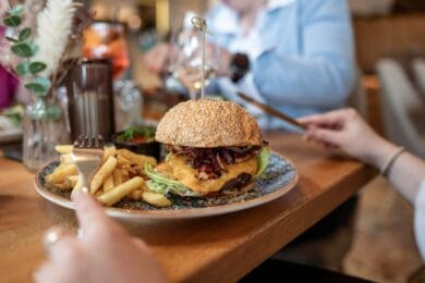 Burger-Genuss im Restaurant Stegerbräu - Radstadt Saftiger Cheeseburger mit Salat, Zwiebeln und Pommes frites auf einem Teller im Restaurant Stegerbräu in Radstadt.