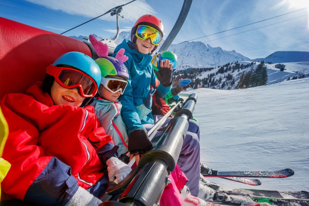 Familie mit Kindern am Sessellift situend bei sonnigem Wintwerwetter vor verschneiter Bergkulisse