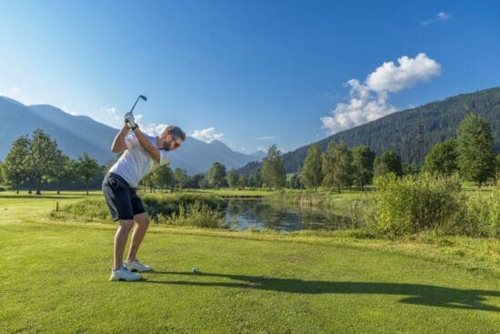 Golf Urlaub - Golfclub Radstadt - Partnerhotel Stegerbräu Ein Golfer beim Abschlag am Golfplatz in Radstadt- im Hintergrund die Berge der Hohen Tauern