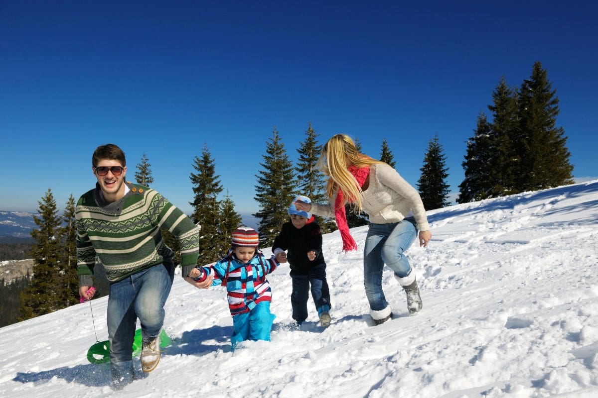 Familie mit zwei Kindern käuft gemeinsam durch den Schnee bei sonnigem Winterwetter in den Bergen